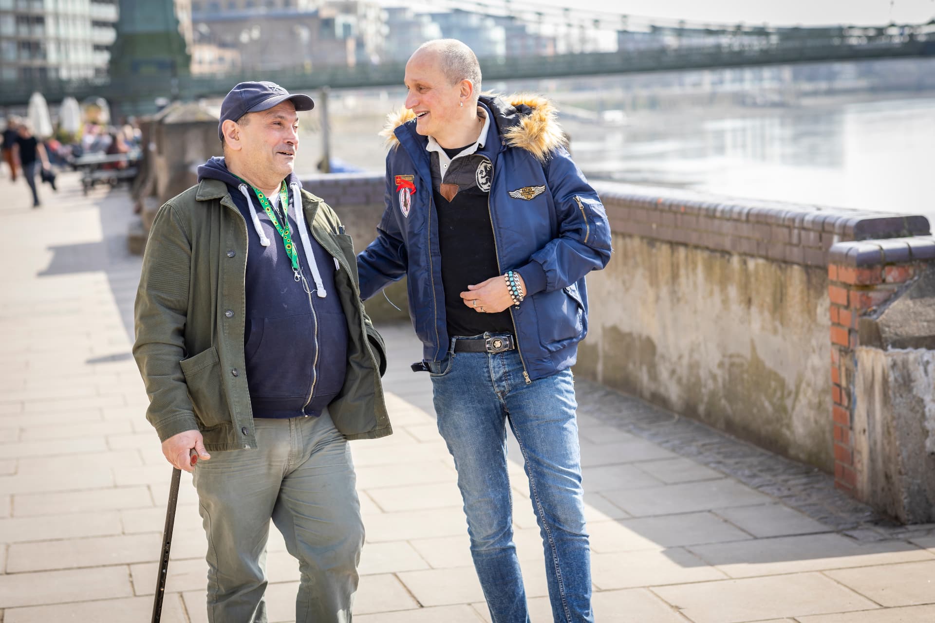 A companion walking and chatting with an older man along the riverside while his family carer takes a break