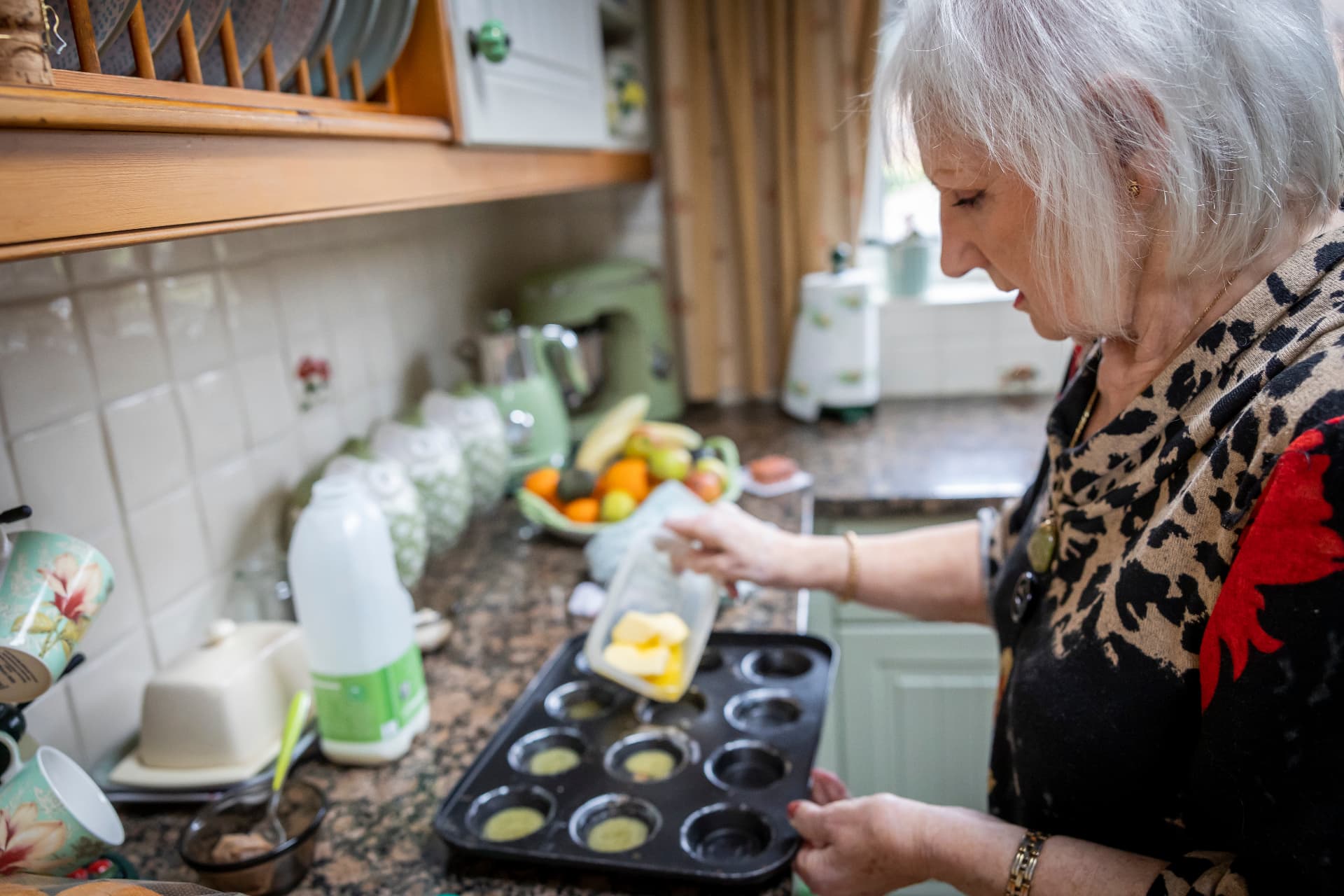 An older woman preparing a meal in her own kitchen with support from a companion