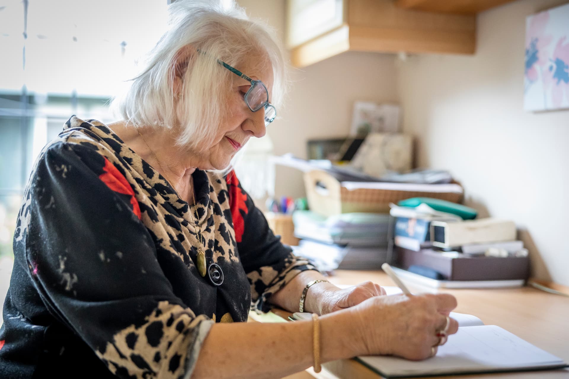 An older woman writing at her desk during a check-in visit that is reported back to her family