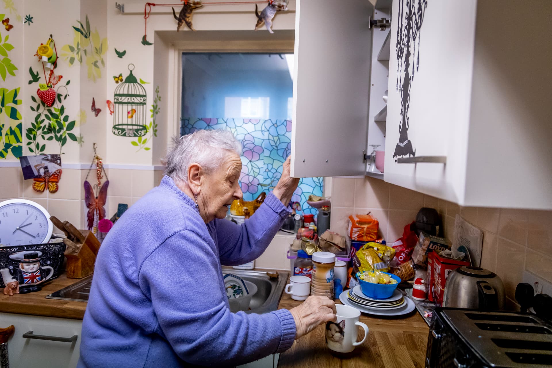 An older woman reaching into her kitchen cupboard for a mug in her own home in Stevenage