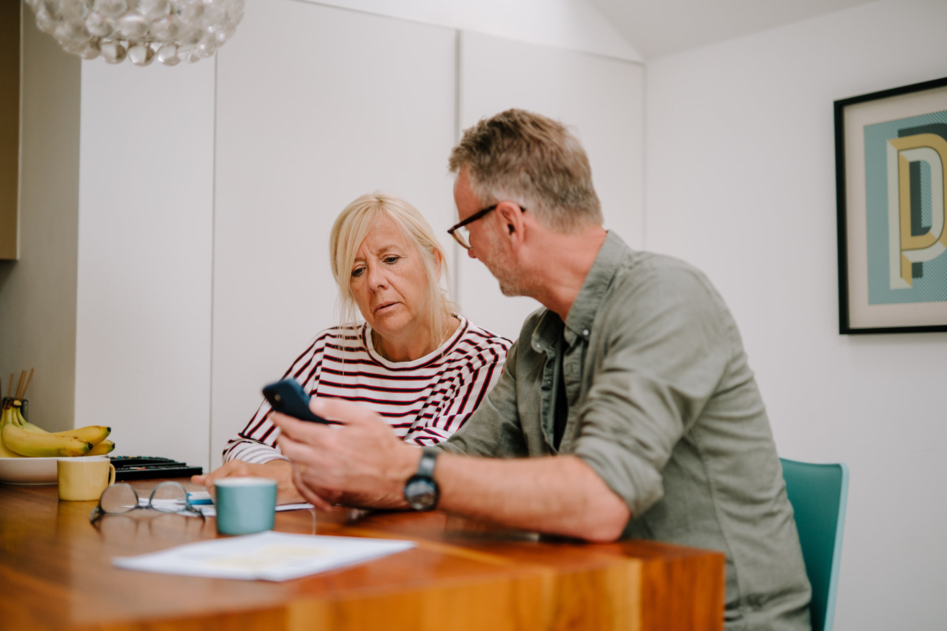 An older couple at their kitchen table going through household paperwork with help from a companion