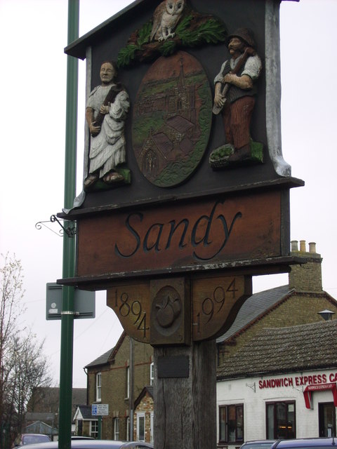 The carved Sandy village sign with local figures and the date 1994
