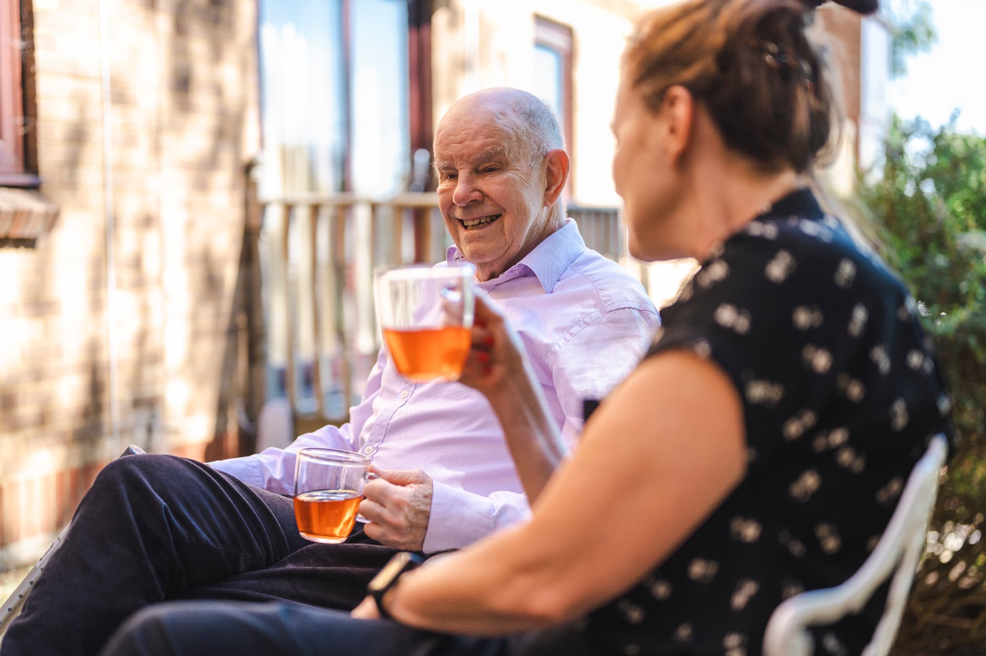 An older man laughing with his companion over cups of tea during a companionship visit at home